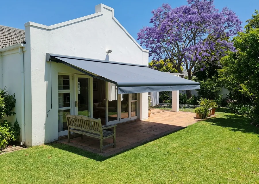 Slate-grey folding-arm awning extended from a white-rendered Menlo Park wall, jacaranda in bloom beyond the lawn